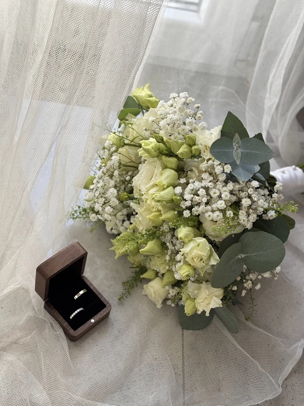 Bridal bouquet of lisianthus, gypsophila and eucalyptus on tulle, beside a ring box
